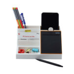 A Pen holder with few pens and a slot for a mobile phone with another compartment for stationary items