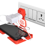 A smartphone is held in red, 3D-printed charging stand that is pluggd into a wall outlet.