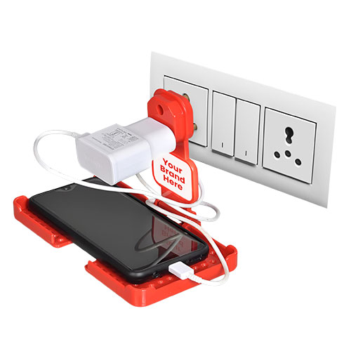 A smartphone is held in red, 3D-printed charging stand that is plugged into a wall outlet.